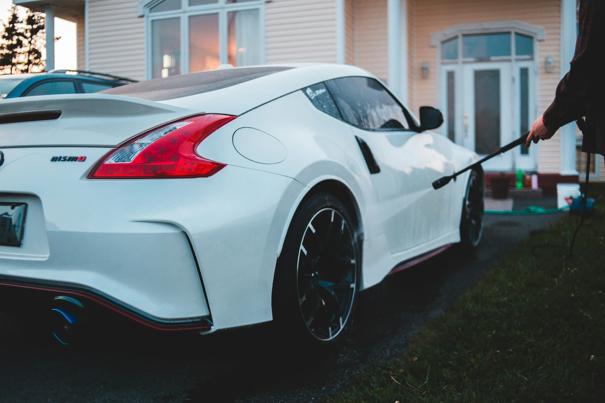 White sports car being pressure washed outside a house