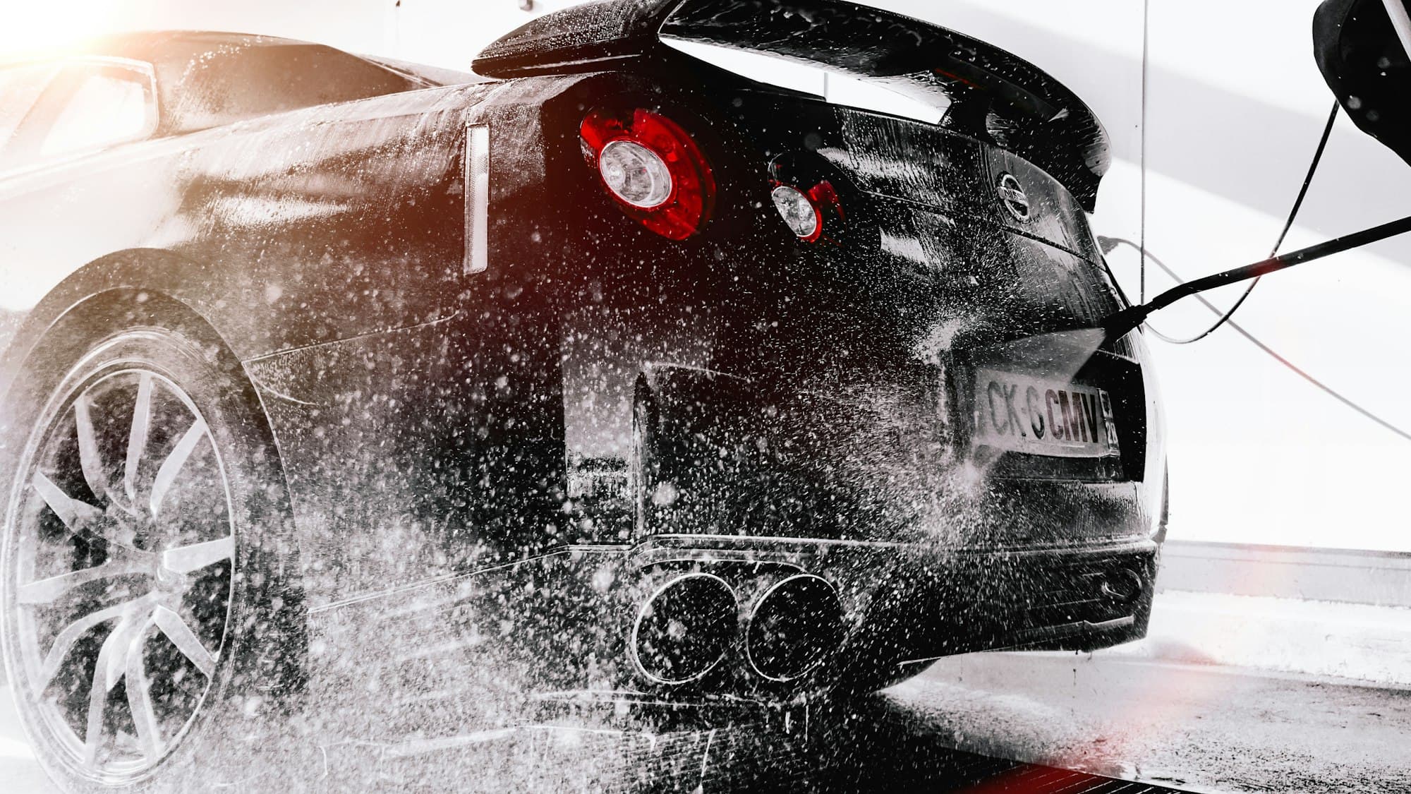Black sports car being rinsed during a professional wash