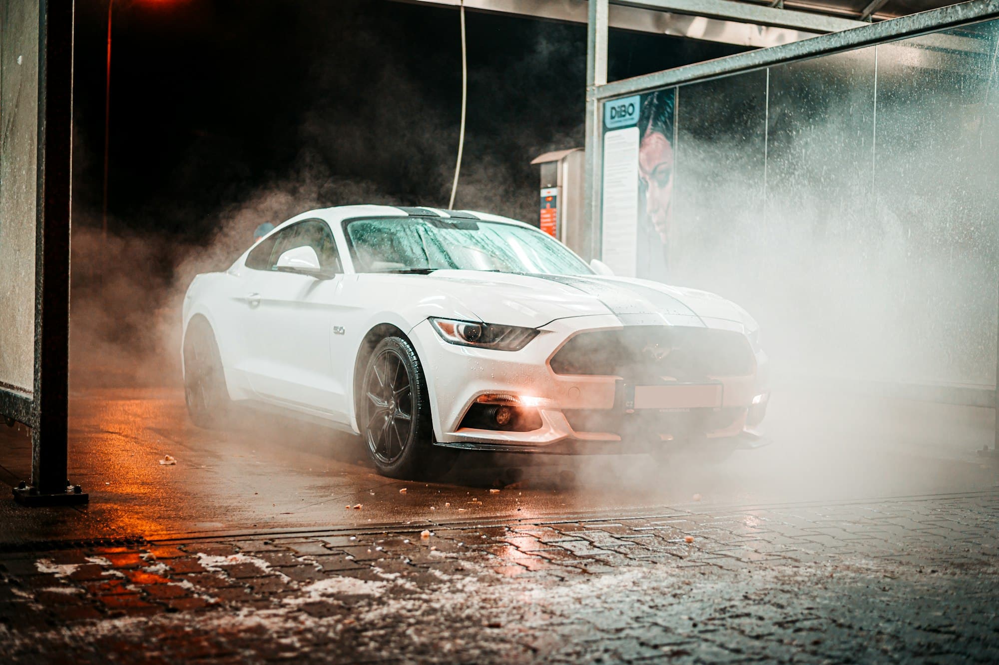 White sports car being washed in a steamy wash bay