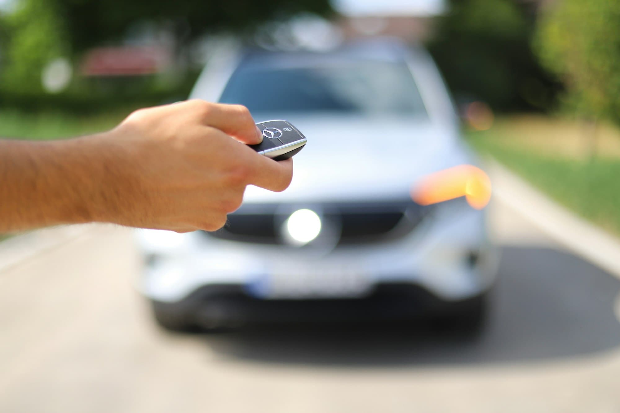 Hand holding a car key fob in front of a car