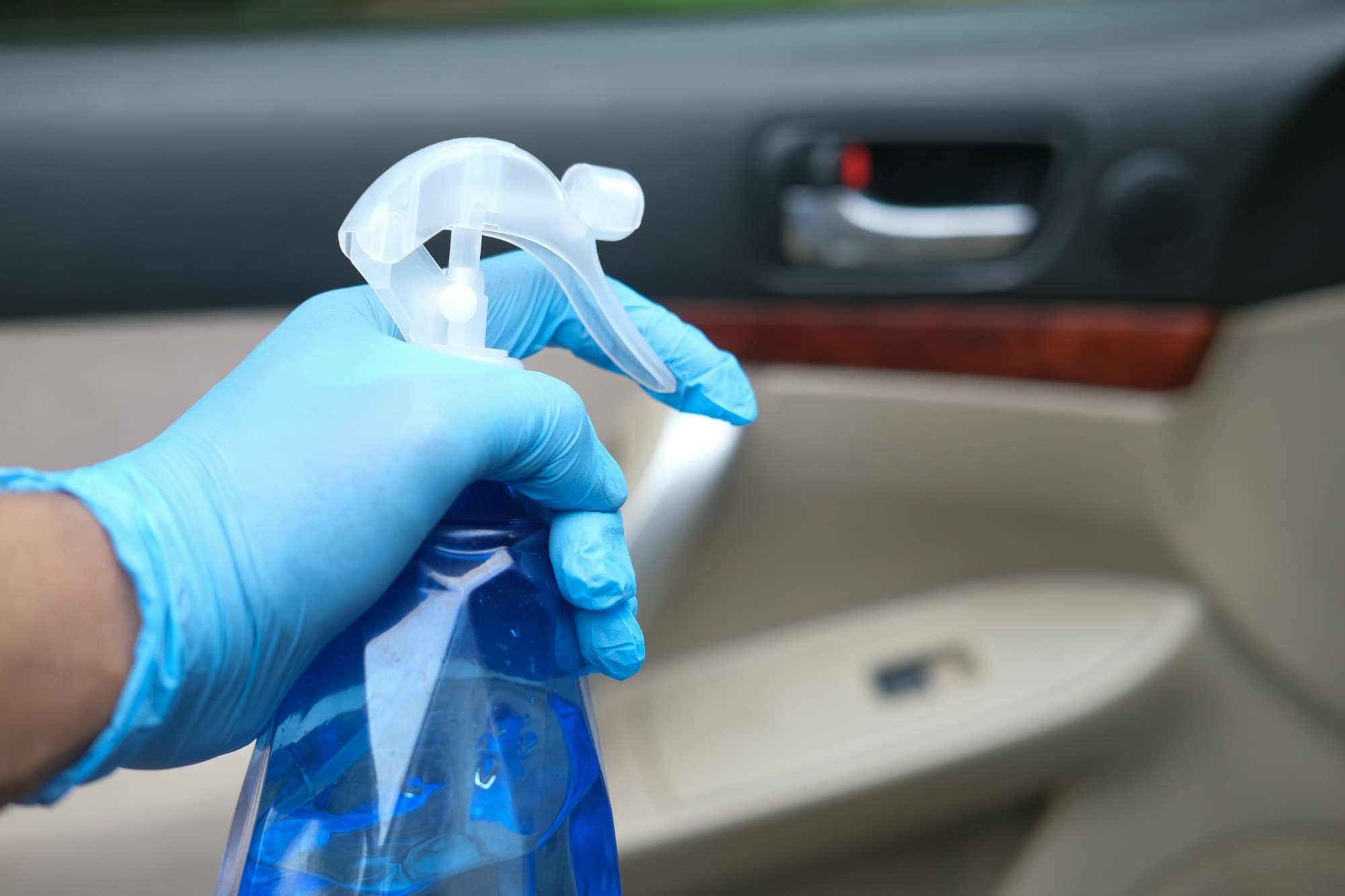 Gloved hand spraying cleaner on a car door panel