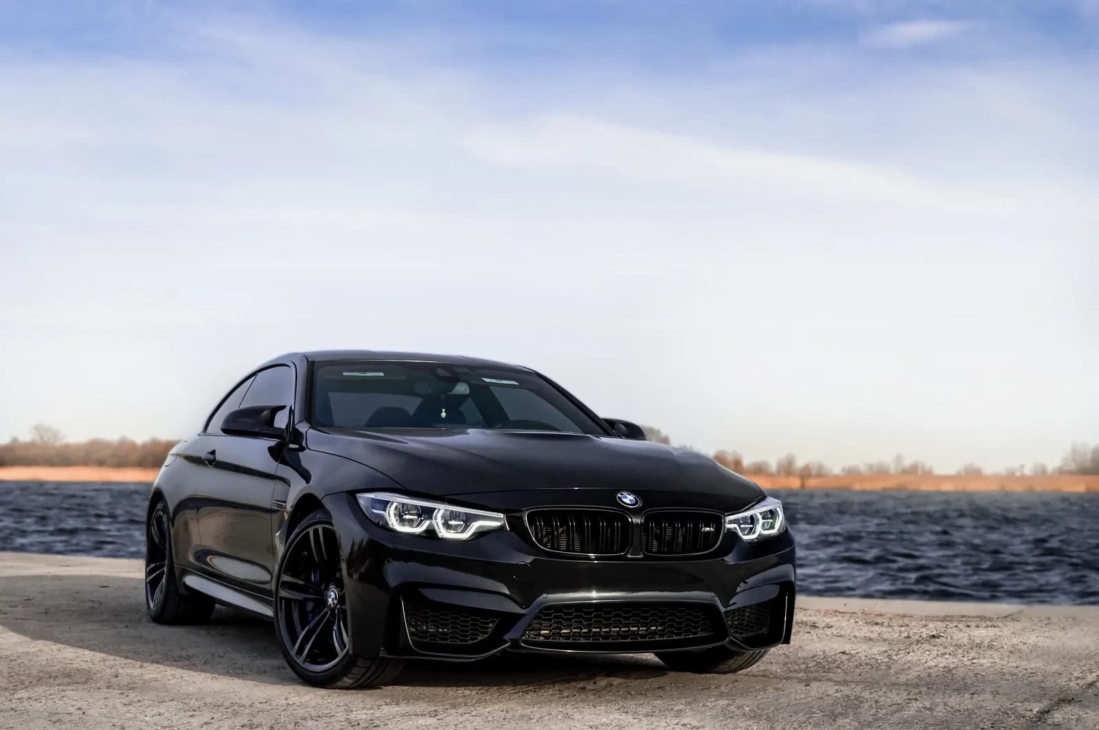 Black BMW M4 parked by the water with a freshly detailed gloss finish